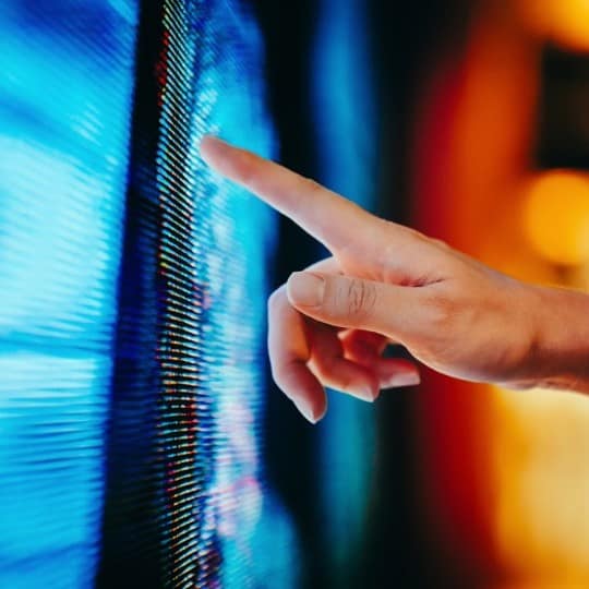 A person's index finger touches a bright blue and white pixelated digital screen.
