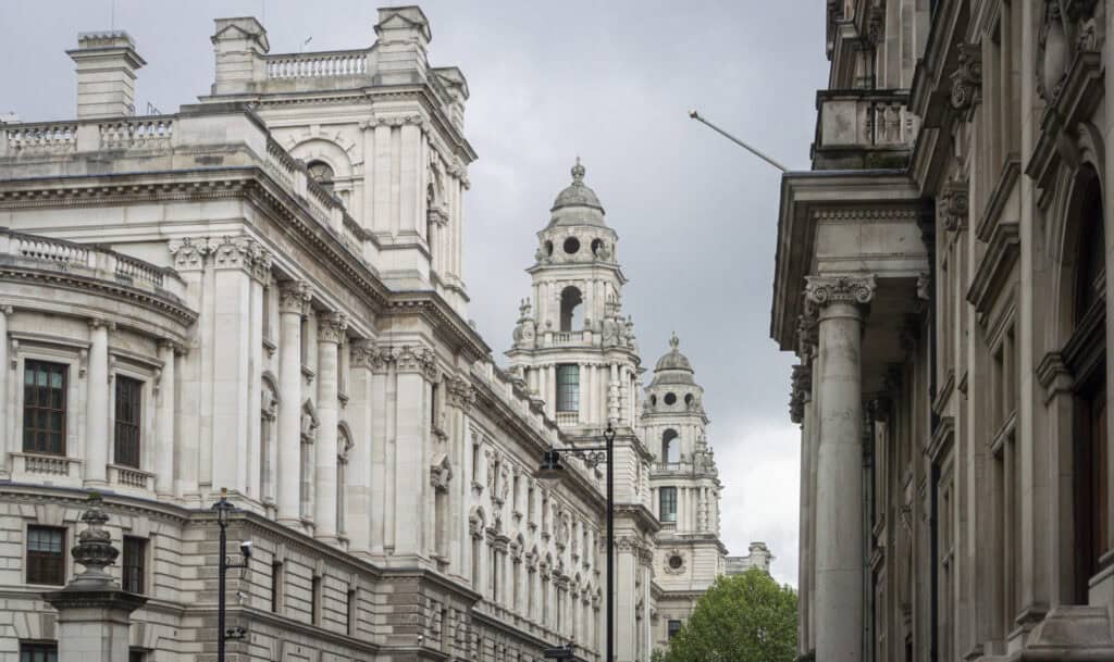 Ornate, light grey stone buildings with classical columns, balustrades, and domed towers under an overcast sky.