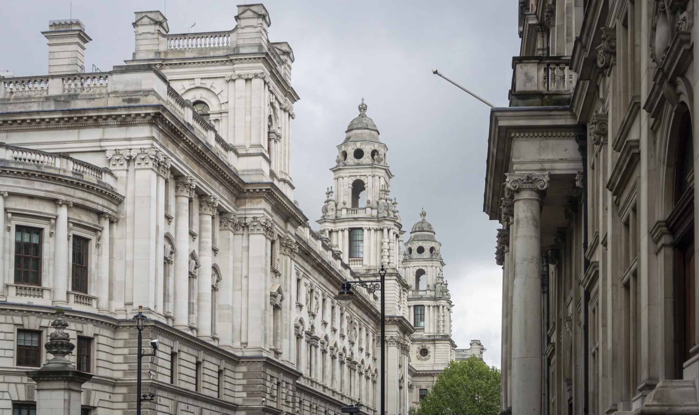 Ornate, light grey stone buildings with classical columns, balustrades, and domed towers under an overcast sky.