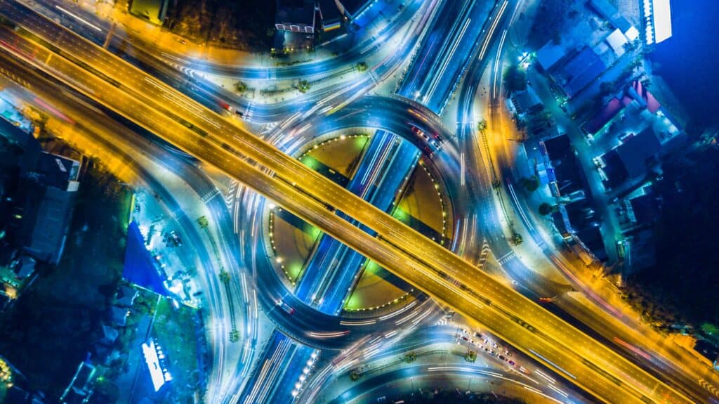 Aerial view of a complex highway interchange at night with vehicle light trails.