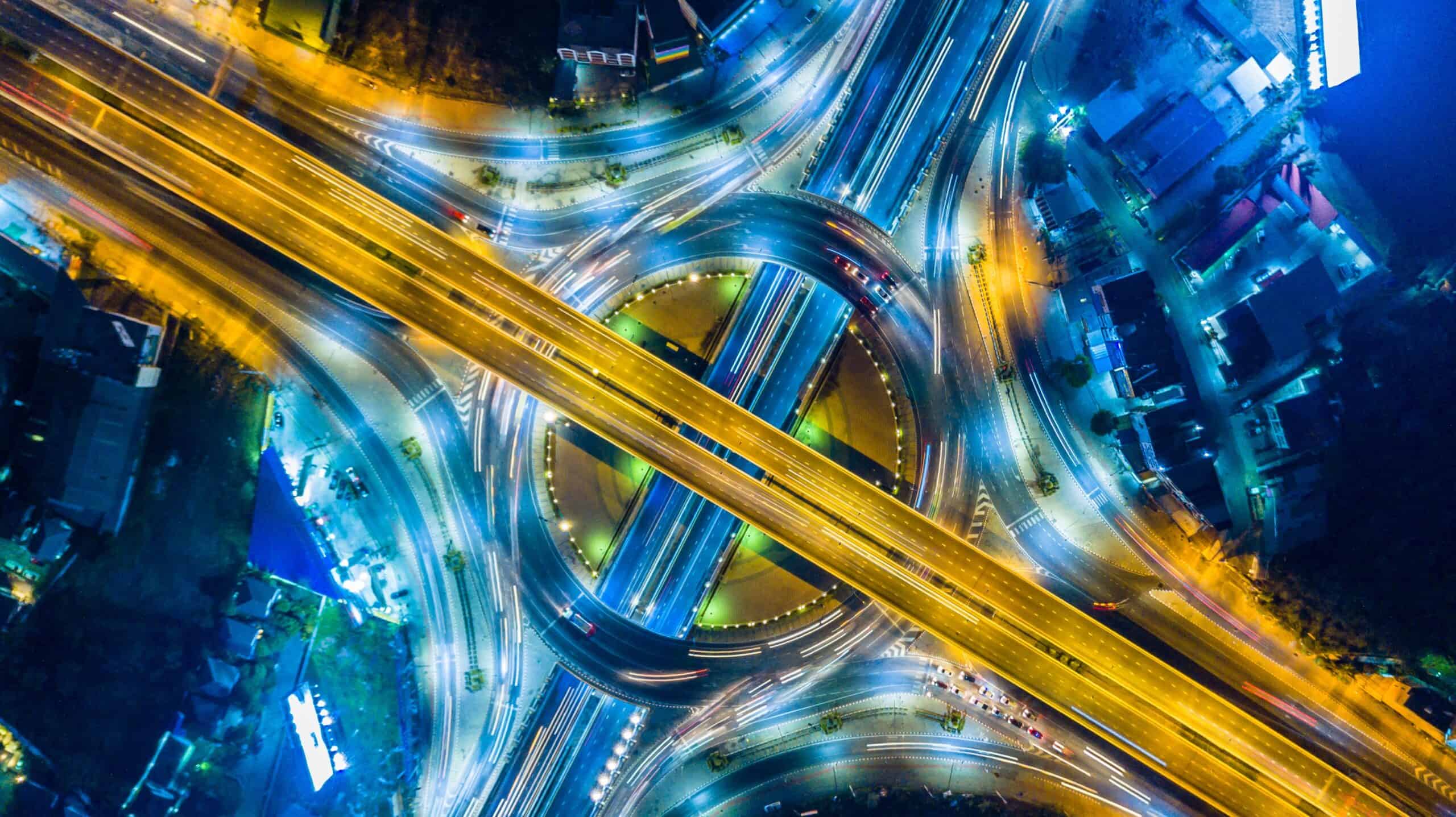 Aerial view of a complex highway interchange at night with vehicle light trails.
