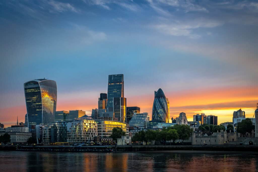 Panoramic view of London's cityscape at sunset, featuring the Walkie-Talkie building, The Gherkin, and the Tower of London along the River Thames.