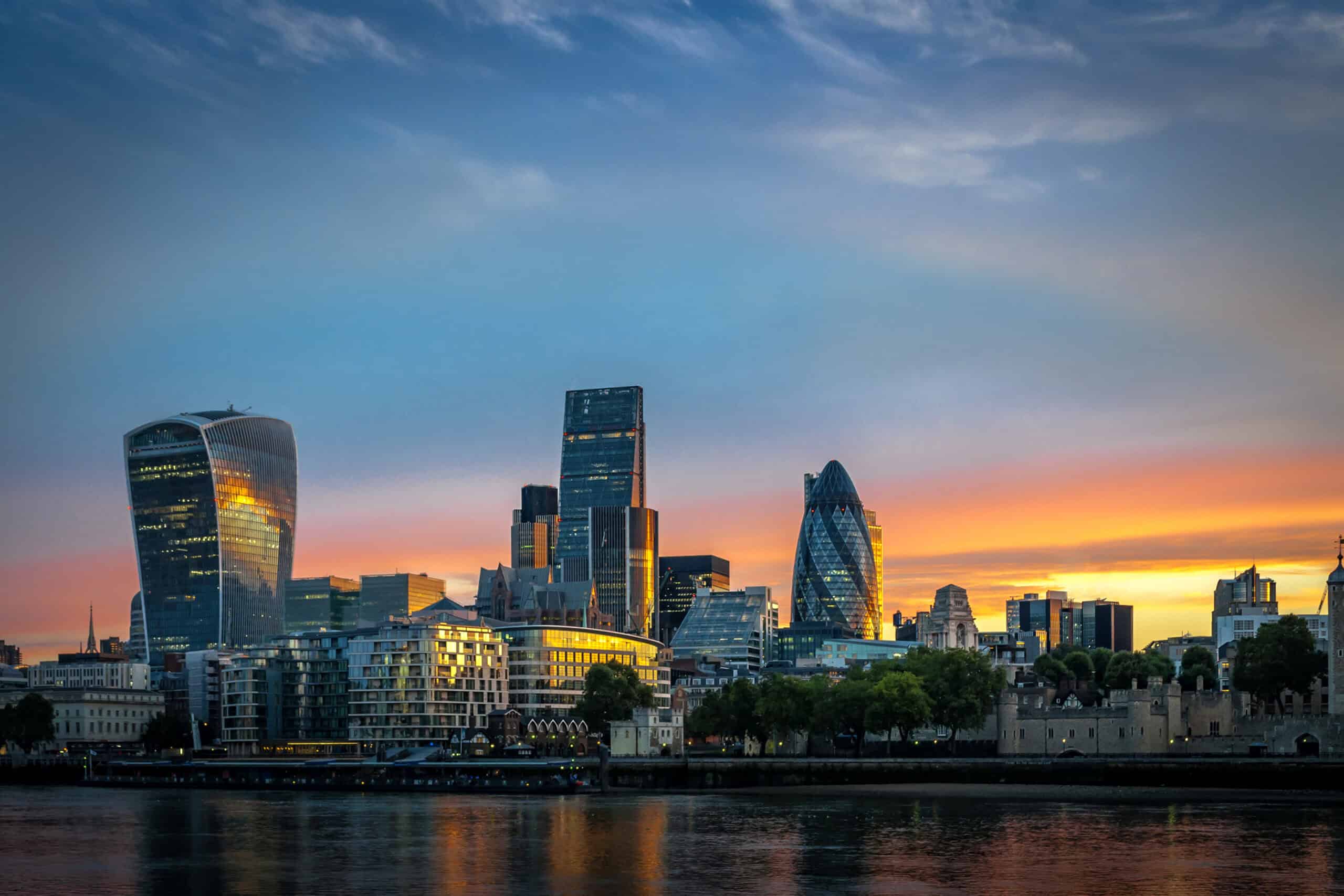 Panoramic view of London's cityscape at sunset, featuring the Walkie-Talkie building, The Gherkin, and the Tower of London along the River Thames.