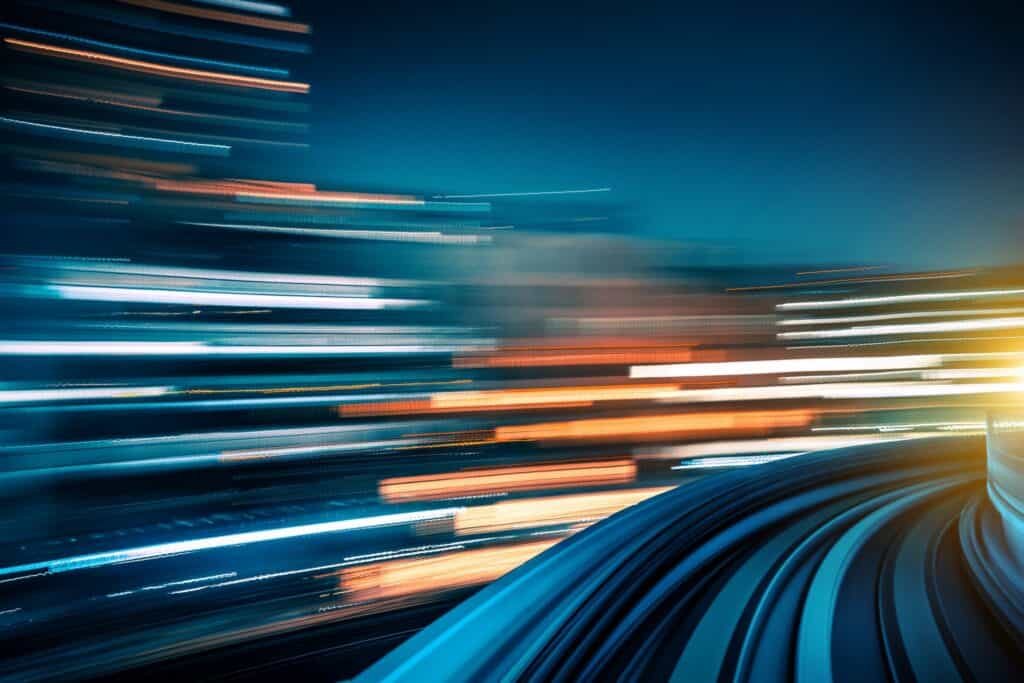 Abstract image showing light trails in white, orange, and blue against a dark background, with a curved blue structure in the foreground, conveying high-speed motion.