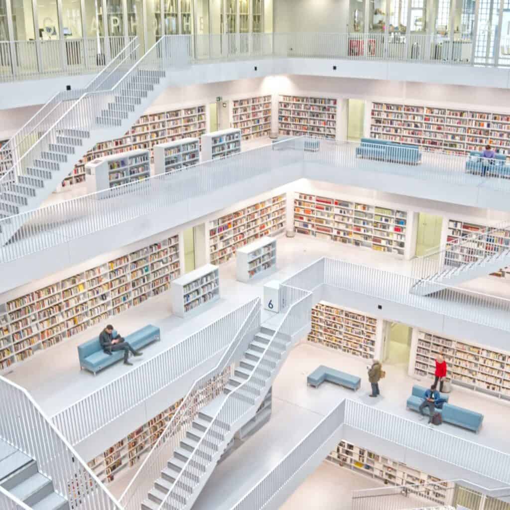 High-angle view of a multi-level, white modern library with numerous staircases, bookshelves, and a few people reading or resting.