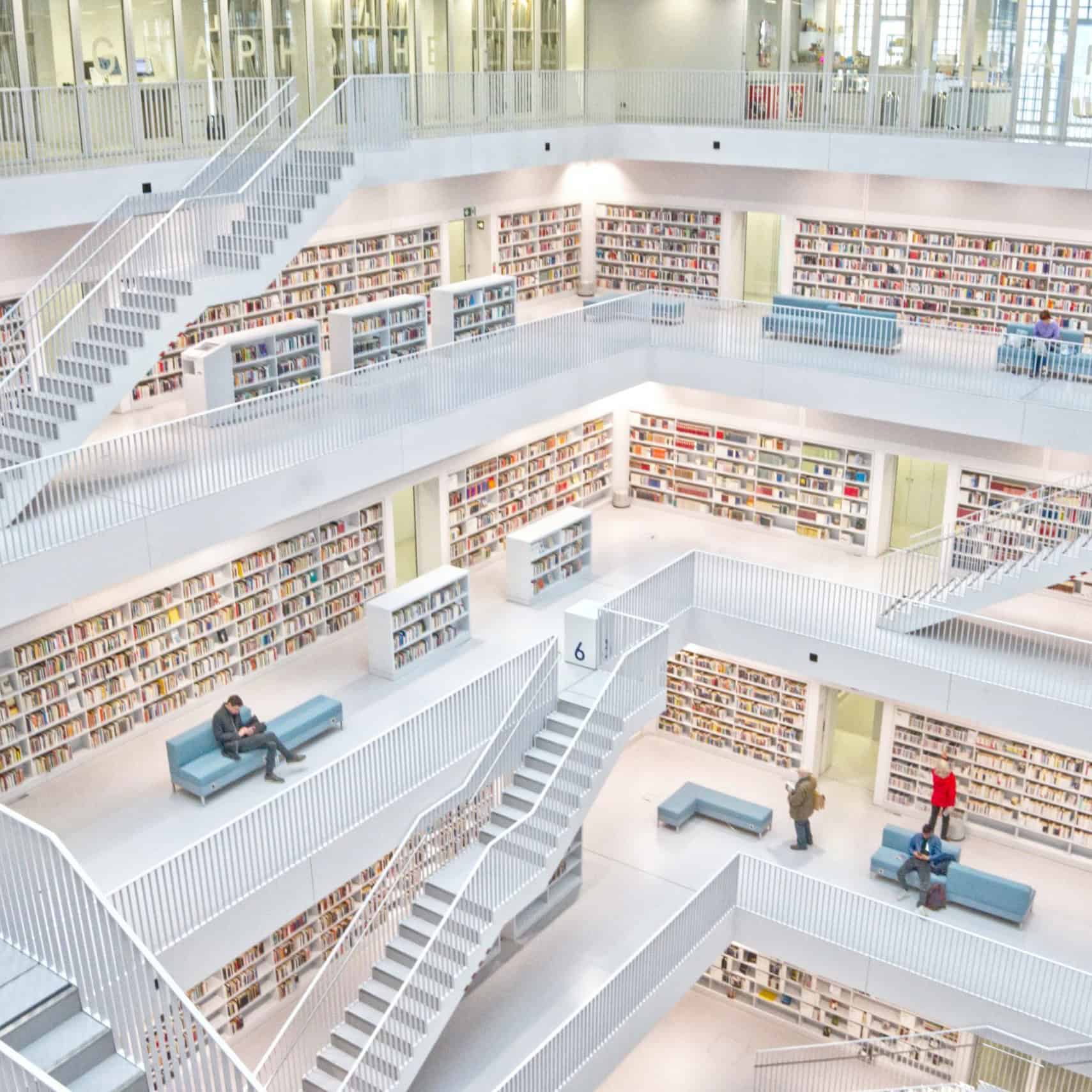 High-angle view of a multi-level, white modern library with numerous staircases, bookshelves, and a few people reading or resting.