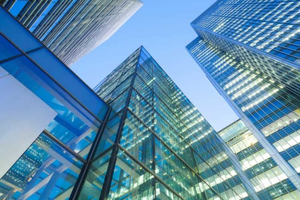 Low-angle view of multiple modern glass skyscrapers with reflective windows and a clear blue sky.
