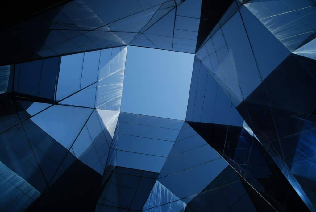 Abstract view looking up at a modern building with angular blue glass panels and a square of clear sky.