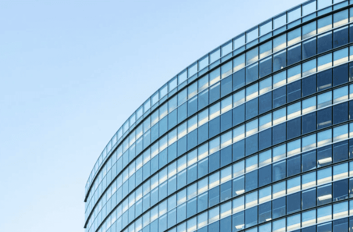 A low-angle view of a modern building with a curved glass facade reflecting the blue sky.