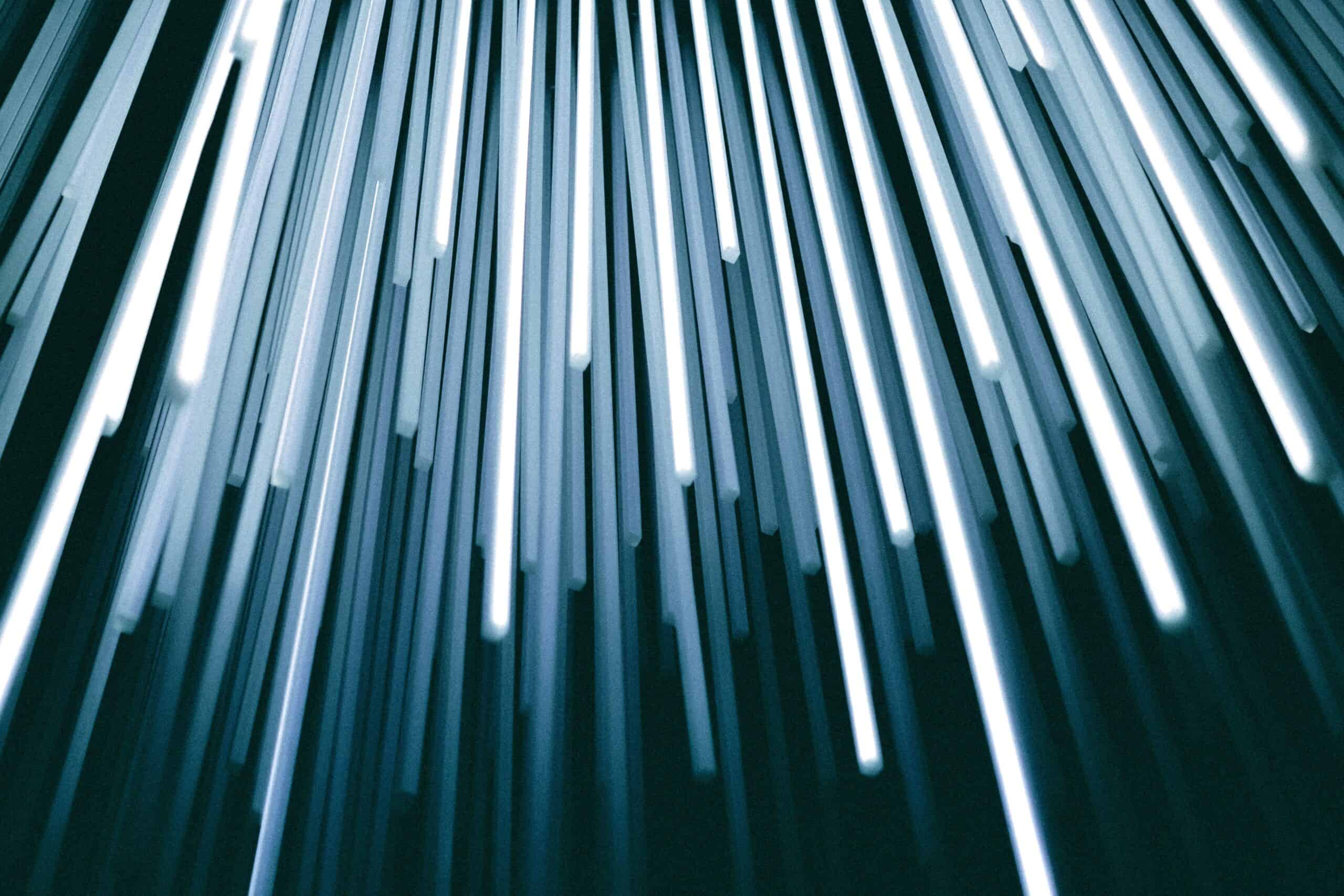 Abstract image of numerous glowing white and blue-grey vertical rods against a dark background.