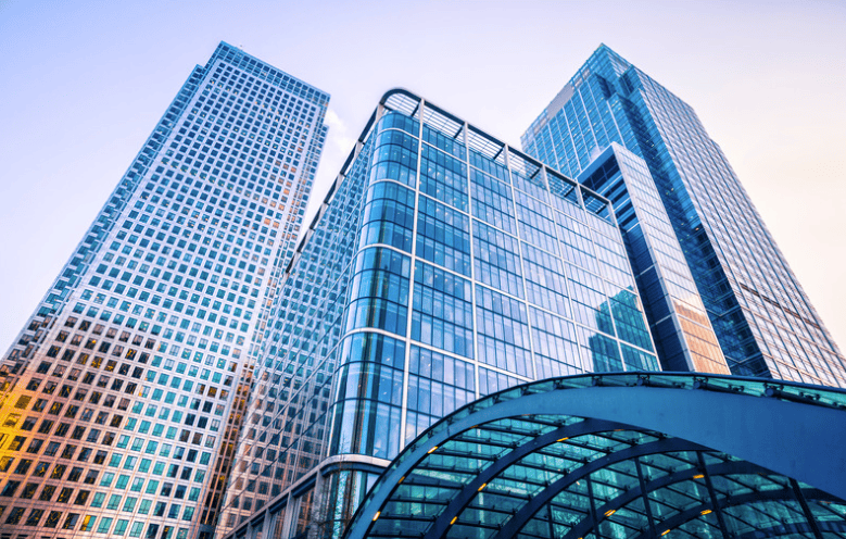 A low-angle view of three modern glass skyscrapers and a curved glass canopy, reflecting the sky.