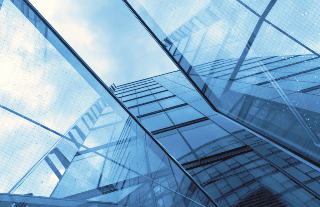Low-angle view of a modern building with blue glass facades reflecting the sky and clouds.