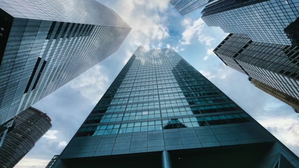 Low-angle view of several modern glass skyscrapers reaching towards a cloudy blue sky.