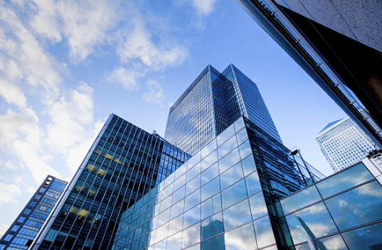 Upward view of multiple modern glass skyscrapers under a blue sky with white clouds.