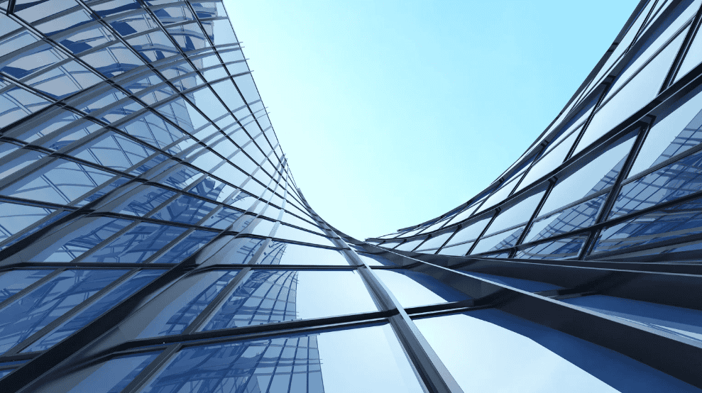 Low-angle view of a modern building with curved, reflective blue glass panels and dark frames against a light blue sky.