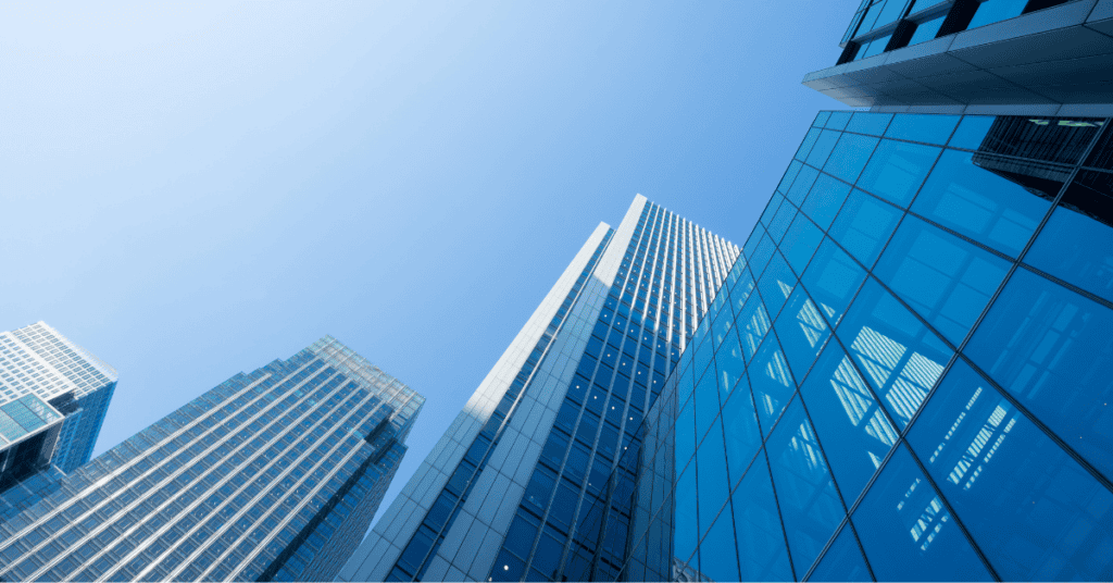 Low-angle view of multiple modern glass and metal skyscrapers under a clear blue sky.