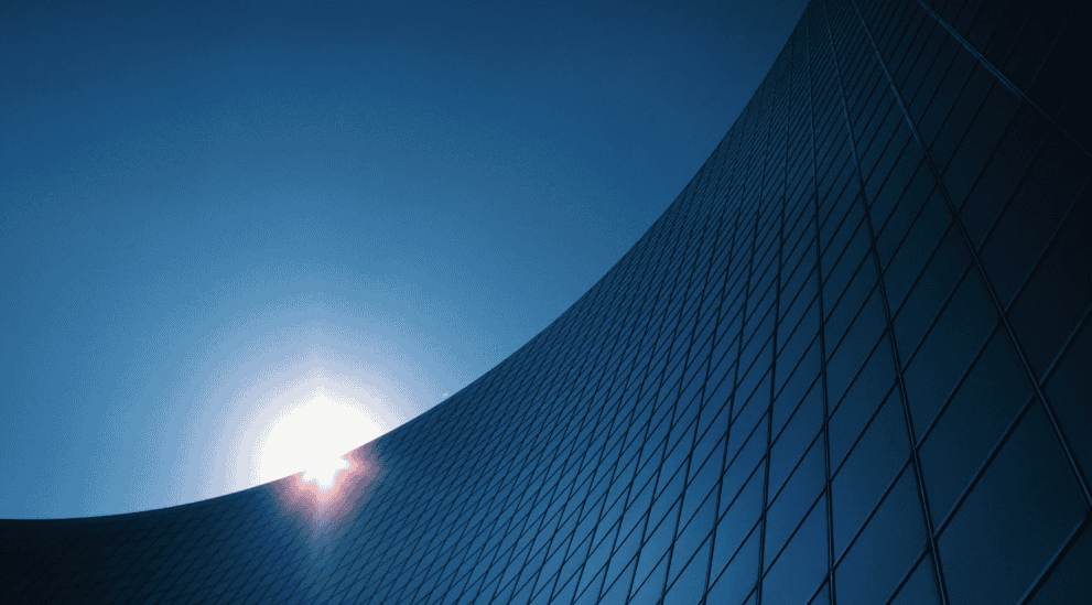 Curved glass building facade with bright sun and blue sky.