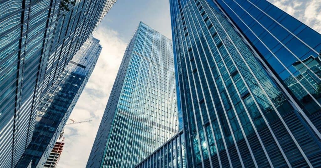 Low-angle view of three towering glass skyscrapers against a cloudy sky, with a construction crane visible.