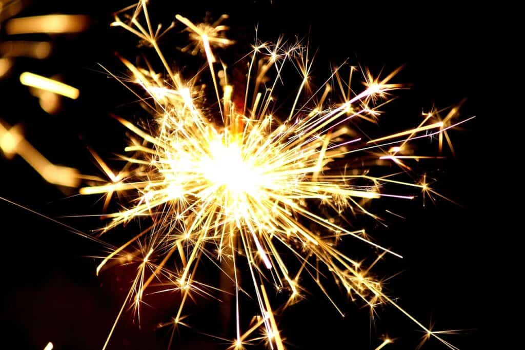 A lit sparkler emitting bright yellow and orange sparks against a dark background.
