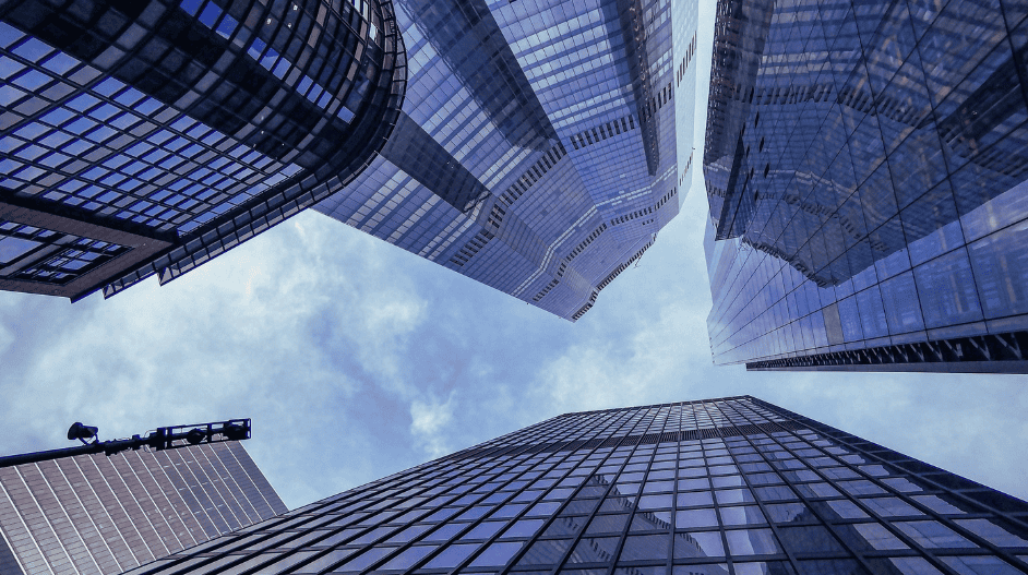 Low-angle view of multiple modern glass skyscrapers reaching into a cloudy sky, with reflective surfaces.