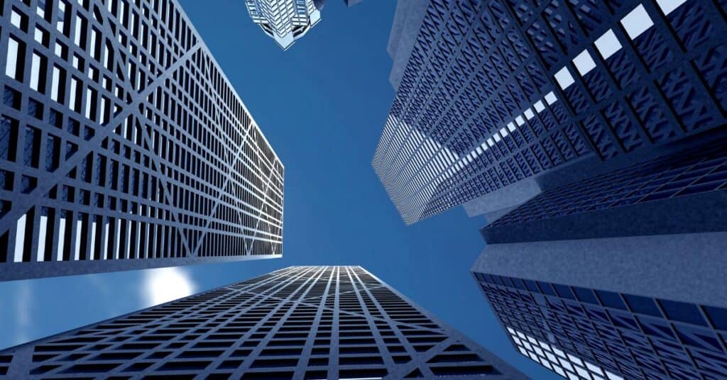 Low-angle view of multiple modern skyscrapers with geometric facades against a clear blue sky.
