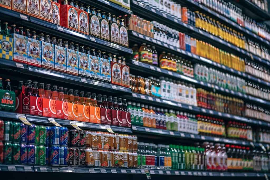 A grocery store aisle with multiple shelves fully stocked with various bottled and canned beverages, including Virgil's sodas, IZZE sparkling juices, Zevia, and Blue Sky.