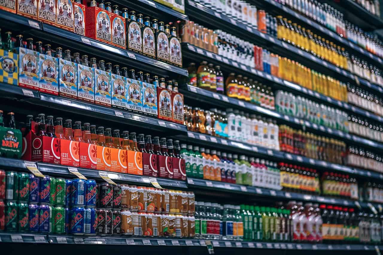 A grocery store aisle with multiple shelves fully stocked with various bottled and canned beverages, including Virgil's sodas, IZZE sparkling juices, Zevia, and Blue Sky.