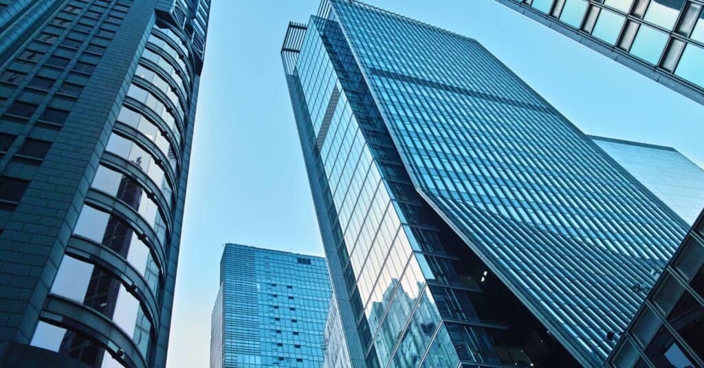Low-angle view of multiple modern skyscrapers with reflective blue glass facades against a clear blue sky.