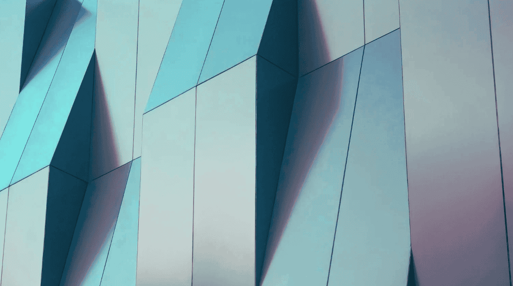Close-up of a modern building facade with geometric panels in shades of blue, teal, and grey, creating an abstract pattern of light and shadow.