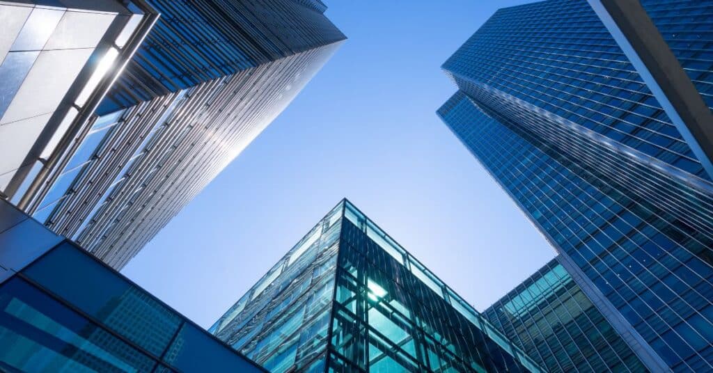 Low-angle view of multiple blue glass skyscrapers against a clear blue sky, with sun reflections.