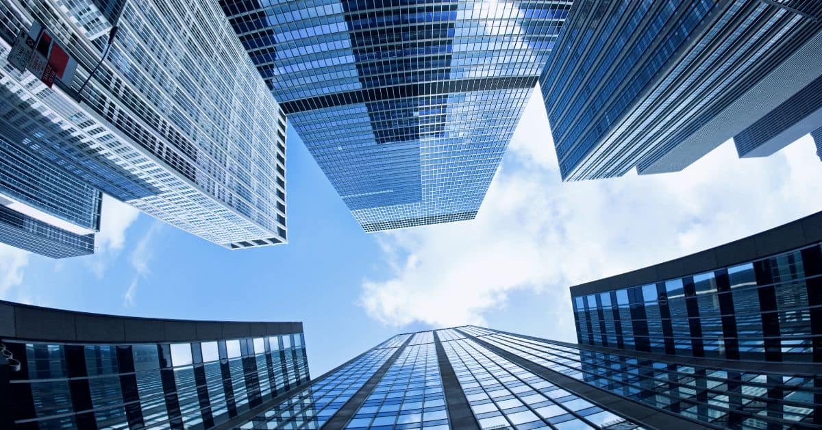 Low-angle view of multiple modern glass skyscrapers against a blue sky with white clouds.