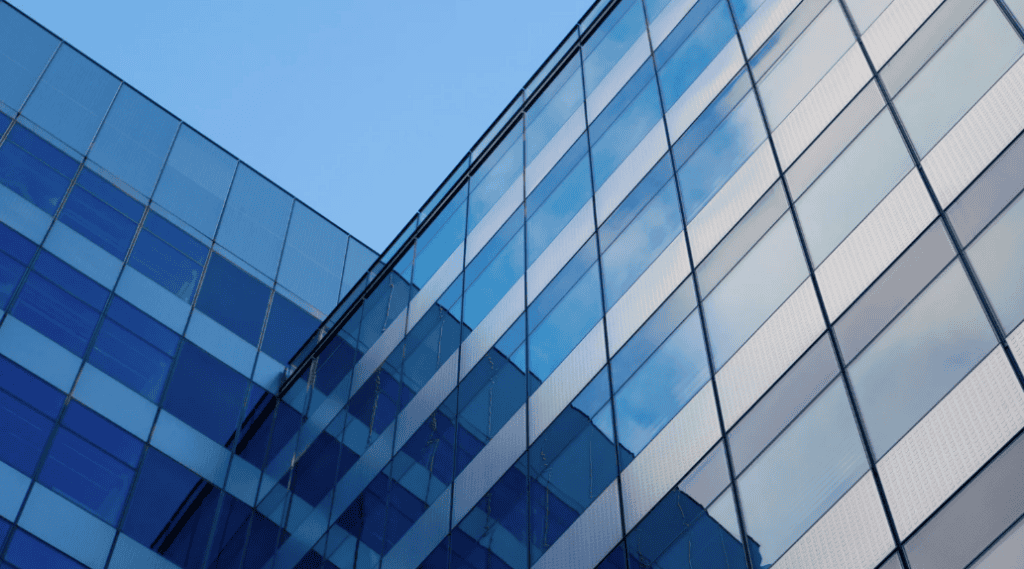 Close-up of a modern building facade with blue glass windows and light grey textured panels reflecting a clear sky.