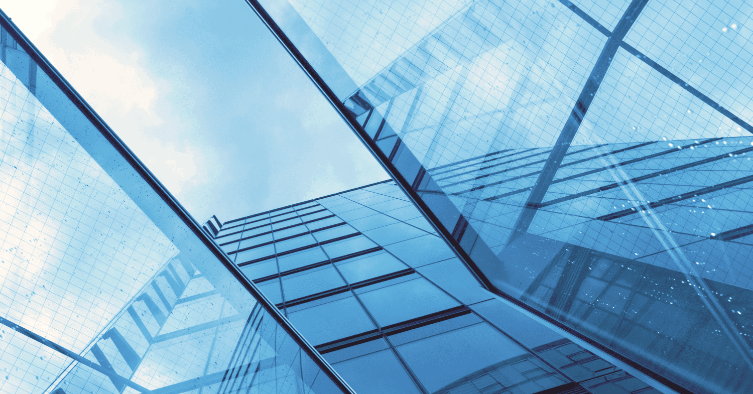 Low-angle view of a modern glass building facade reflecting a blue sky with clouds, showing geometric patterns and reflections.