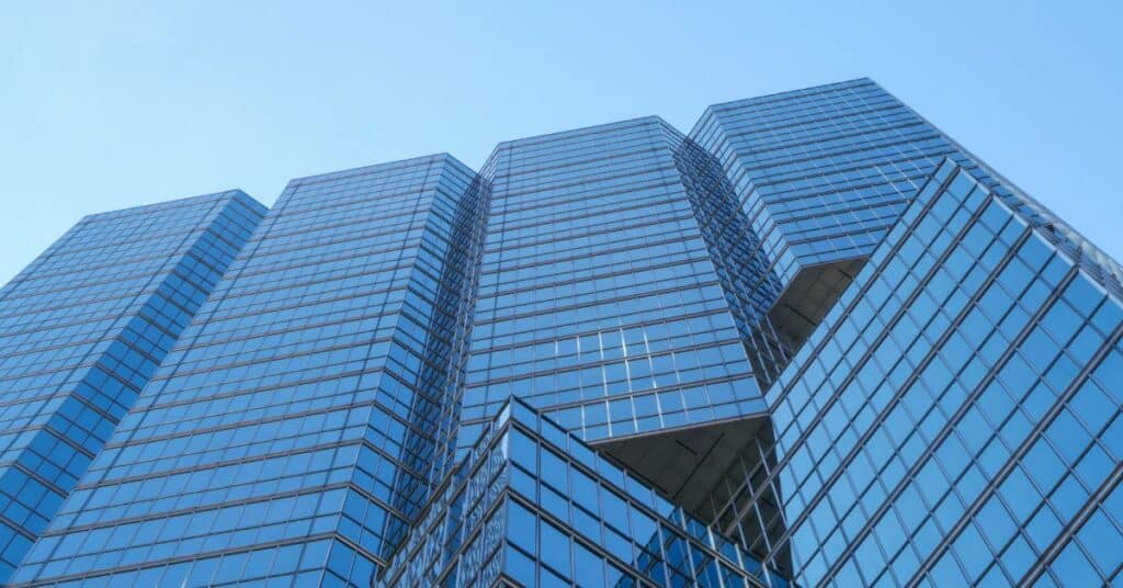 Low-angle view of a modern skyscraper with a reflective blue glass facade against a clear blue sky.