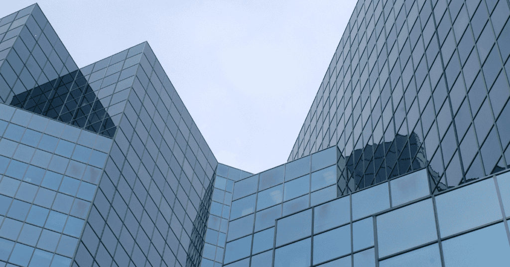 Low-angle view of a modern building with a blue-tinted glass facade, featuring sharp angles and reflective panels.