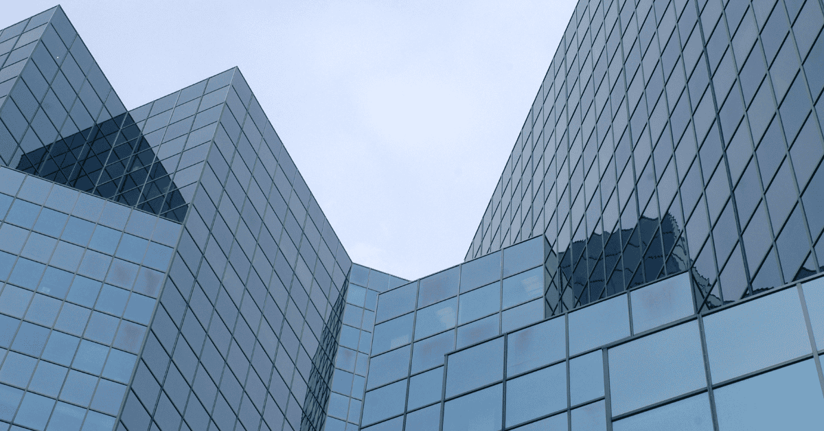 Low-angle view of a modern building with a blue-tinted glass facade, featuring sharp angles and reflective panels.