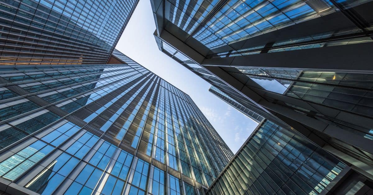 Worm's-eye view of multiple modern glass skyscrapers reflecting the blue sky and other buildings.