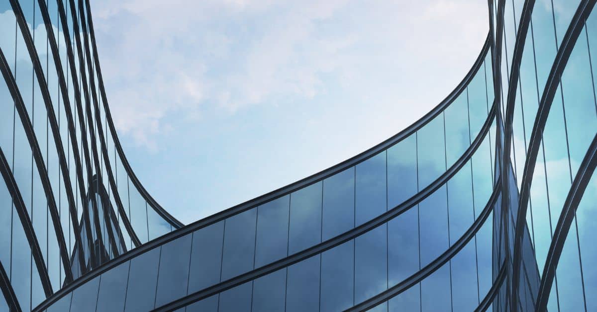 Close-up of a modern building with curved blue glass panels and dark structural lines against a cloudy sky.