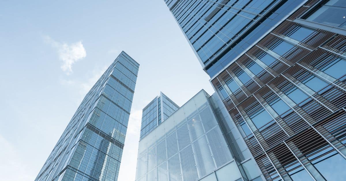 Low-angle view of multiple modern glass skyscrapers against a light blue sky with scattered clouds.
