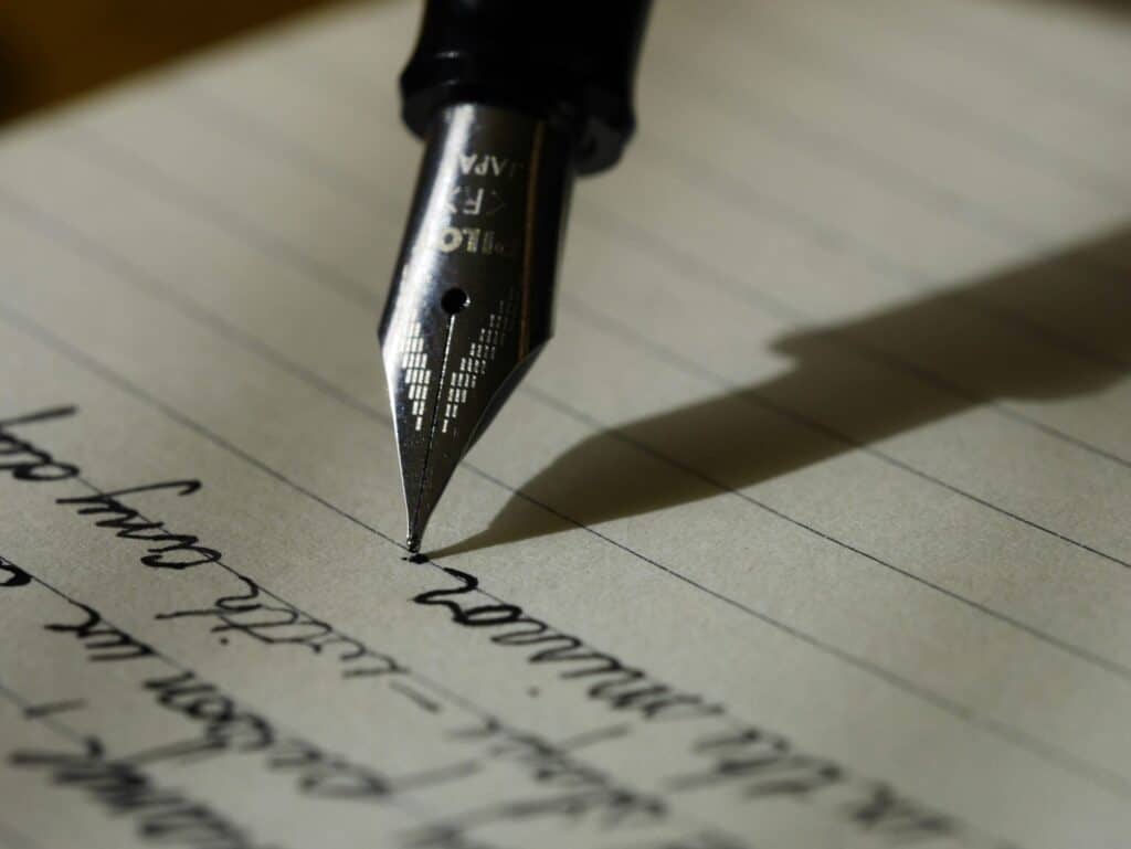 Close-up of a silver fountain pen nib writing black ink on lined paper, with visible text and pen shadow.