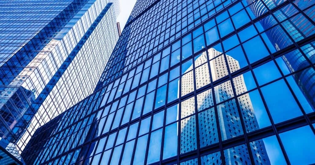 Low-angle view of blue glass skyscrapers reflecting other buildings and a clear sky.
