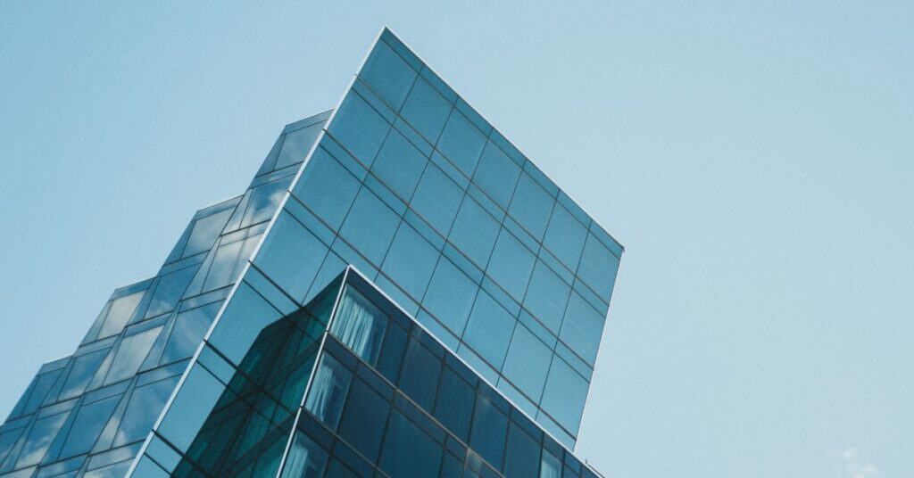 Low-angle view of a modern glass building with a blue reflective facade against a clear sky.