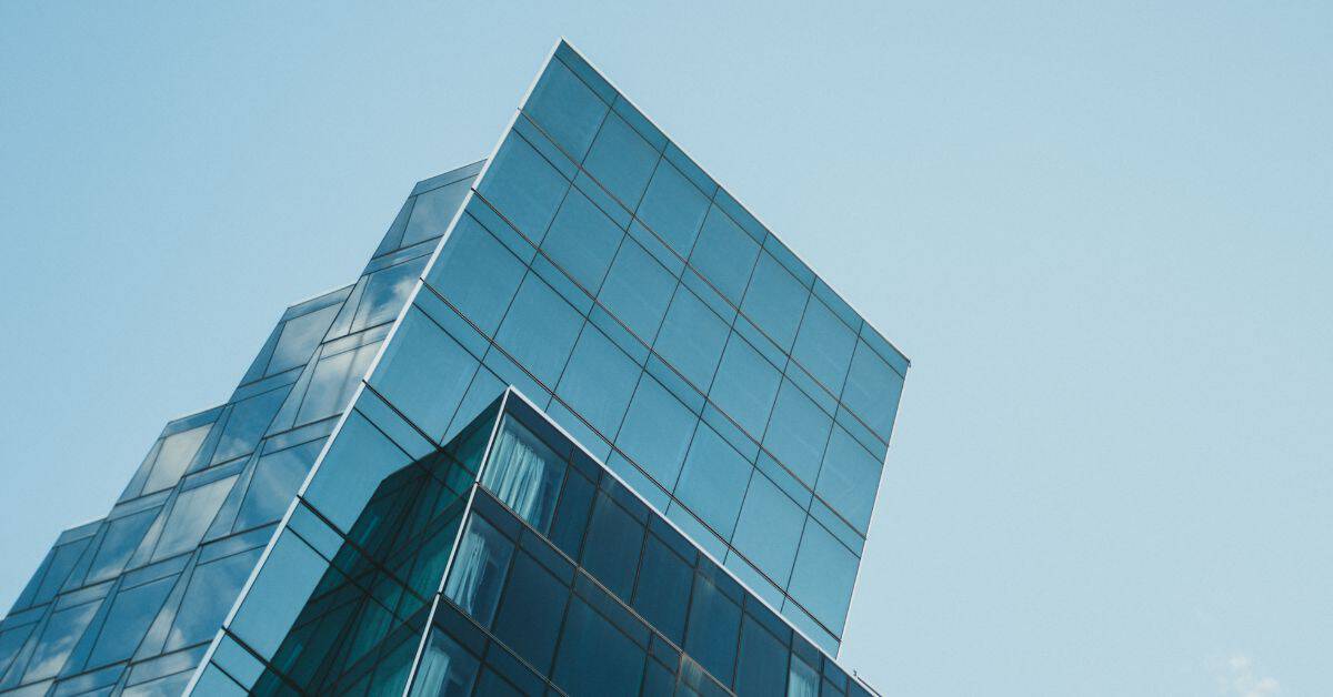 Low-angle view of a modern glass building with a blue reflective facade against a clear sky.