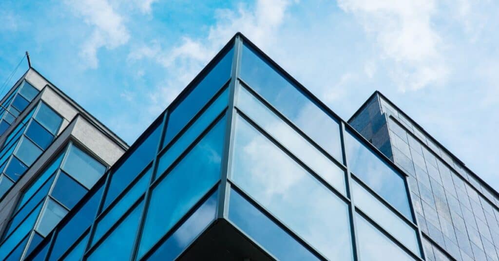 Corner of a modern glass building reflecting a blue sky with white clouds.