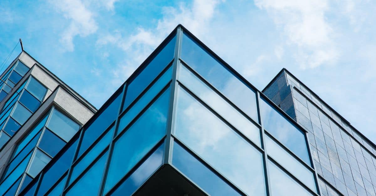 Corner of a modern glass building reflecting a blue sky with white clouds.