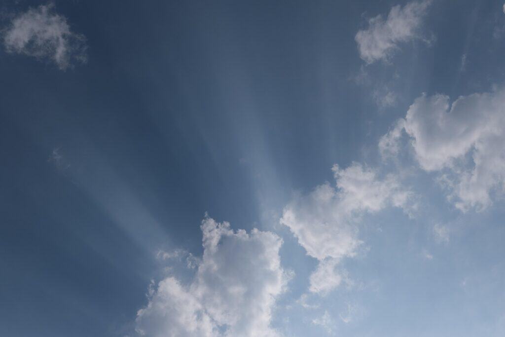 A blue sky with white and grey clouds, from which crepuscular rays of sunlight fan out.