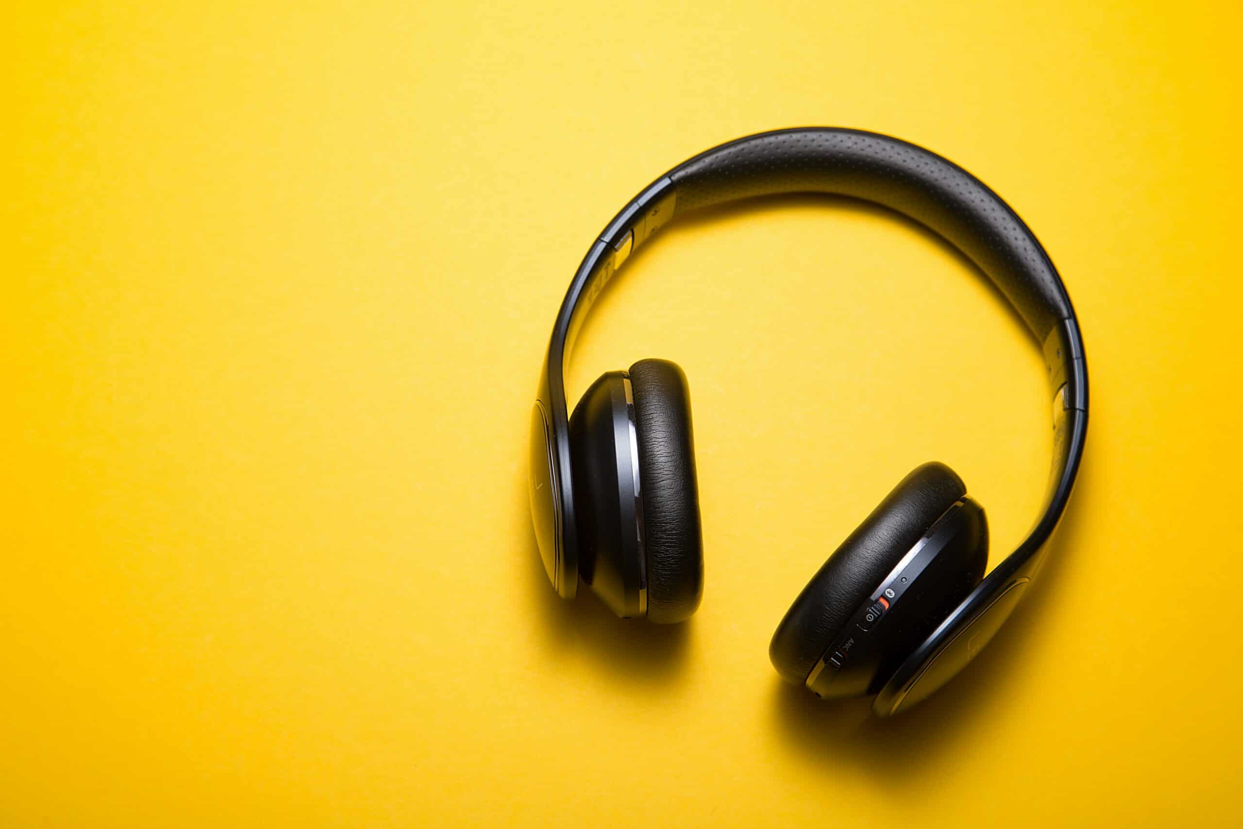 Black over-ear headphones with visible controls resting on a bright yellow background.