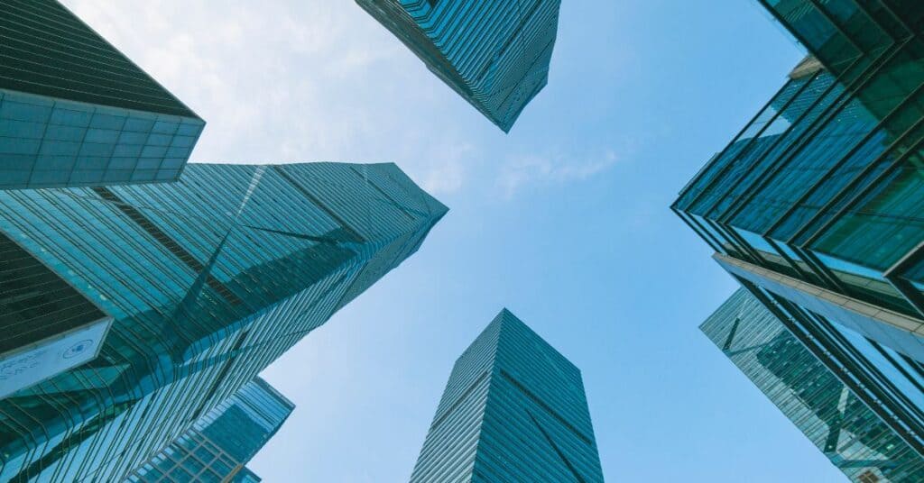 Low-angle view of multiple modern skyscrapers with blue-green glass facades against a clear blue sky.