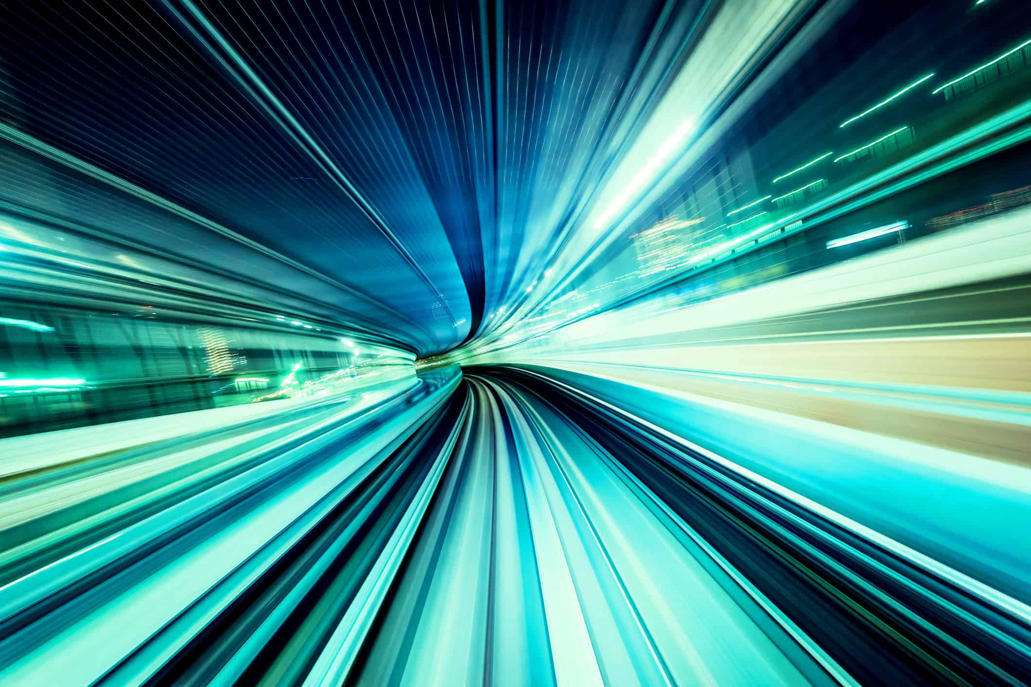 Long exposure photograph from a moving train, showing streaks of blue and teal light from motion blur in a tunnel.