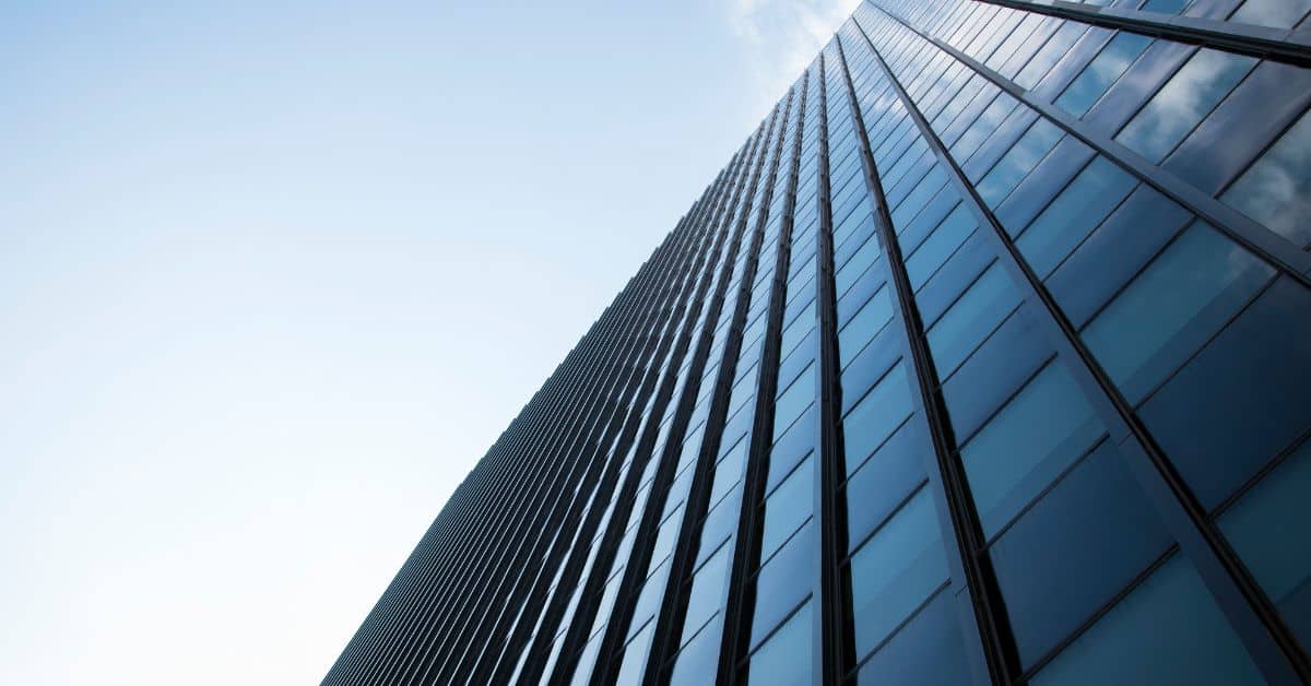 Low-angle view of a tall building with a blue glass facade reflecting the sky.